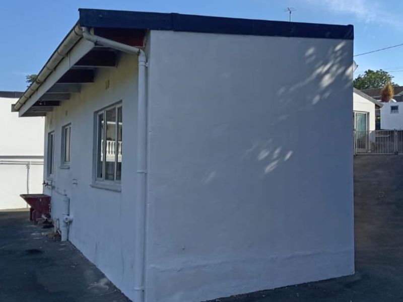 A side view of a detached outbuilding featuring white rendered walls, exposed rafters, and functional guttering systems.