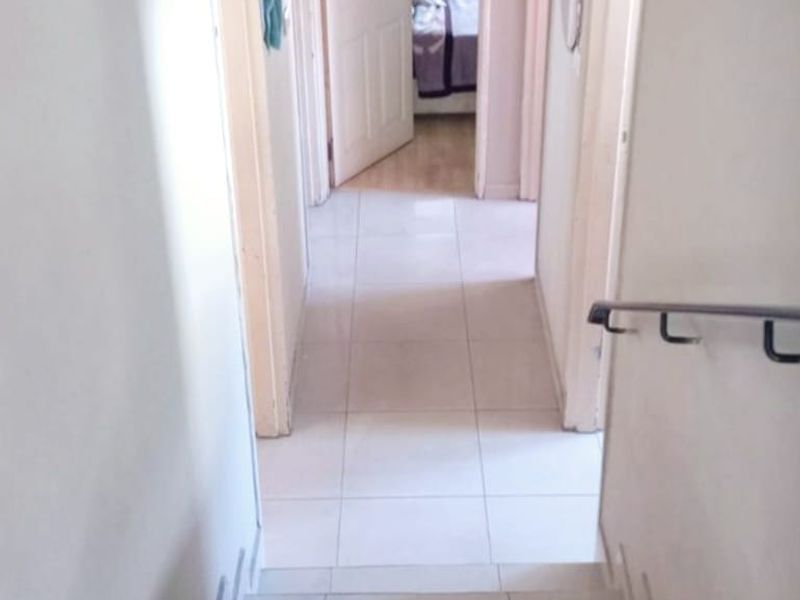 A view looking down a tiled staircase into a hallway with access to multiple rooms, featuring a metal handrail and neutral finishes.