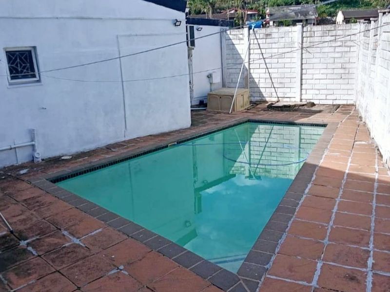 Outdoor pool area featuring a rectangular swimming pool with tiled surround and concrete block boundary walls.