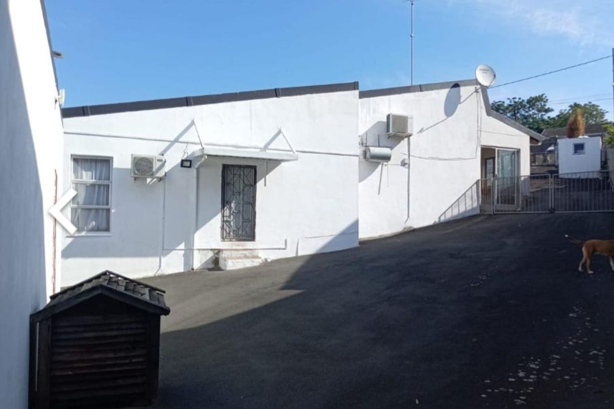 Rear exterior view of the property featuring an asphalt driveway, security gates, and wall-mounted air conditioning units.