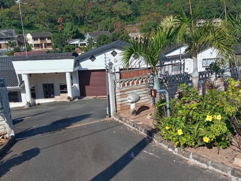 Front exterior view of the property featuring a paved driveway, roller garage door, covered entrance porch, and secure perimeter wall with electric fencing.