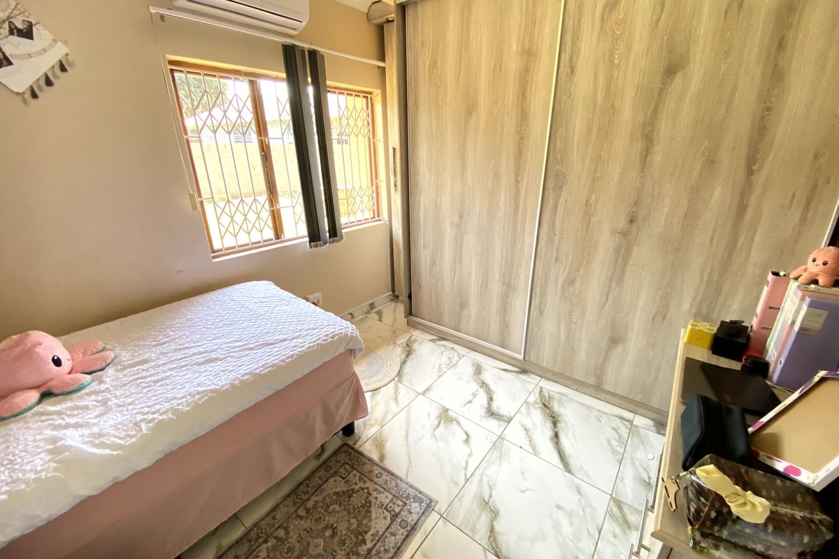 A well-maintained bedroom featuring modern marble-look floor tiles, a large built-in sliding wardrobe, and a wall-mounted air conditioning unit.