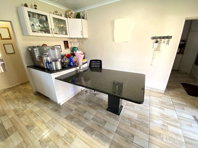 A functional kitchen area featuring a granite-topped breakfast bar, light-toned built-in cabinetry with glass-fronted upper units, and modern wood-look tiled flooring.