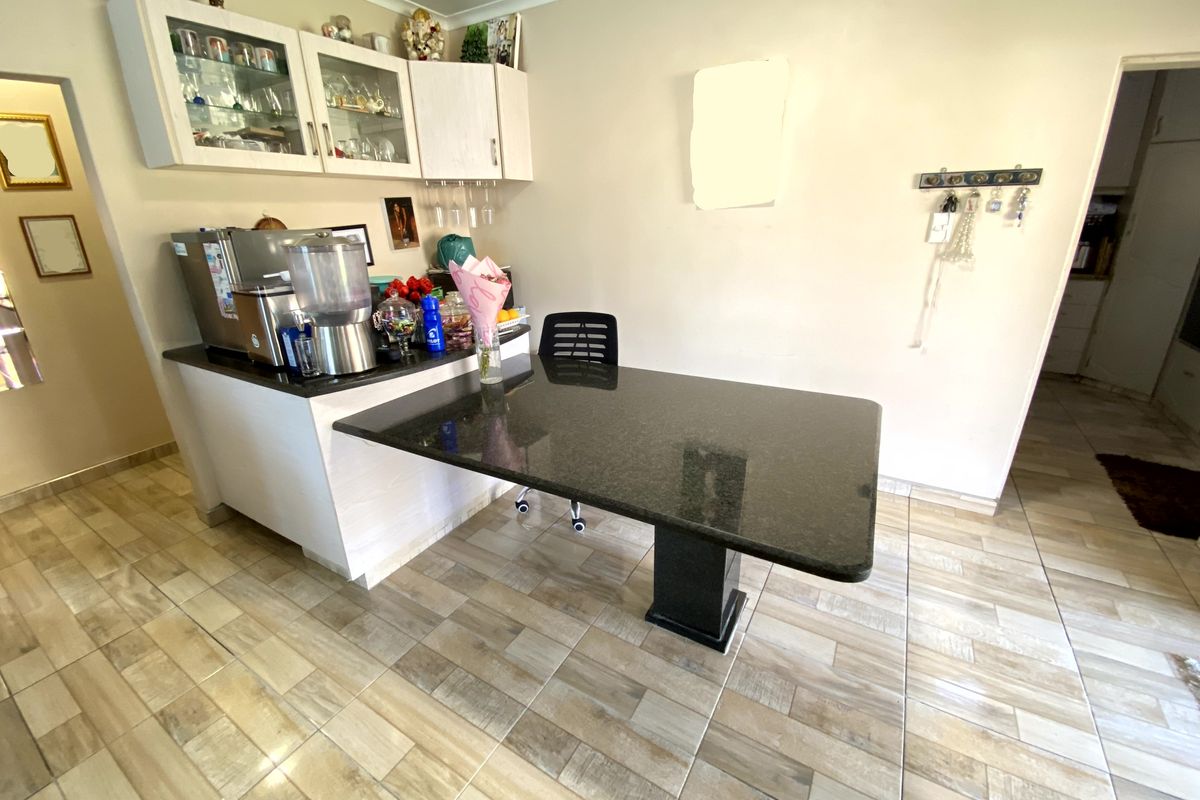 A functional kitchen area featuring a granite-topped breakfast bar, light-toned built-in cabinetry with glass-fronted upper units, and modern wood-look tiled flooring.