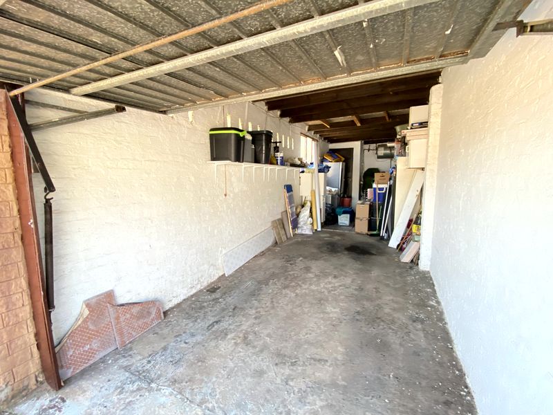 A functional garage space featuring painted brick walls, exposed timber ceiling beams, and a concrete floor, providing ample storage potential.