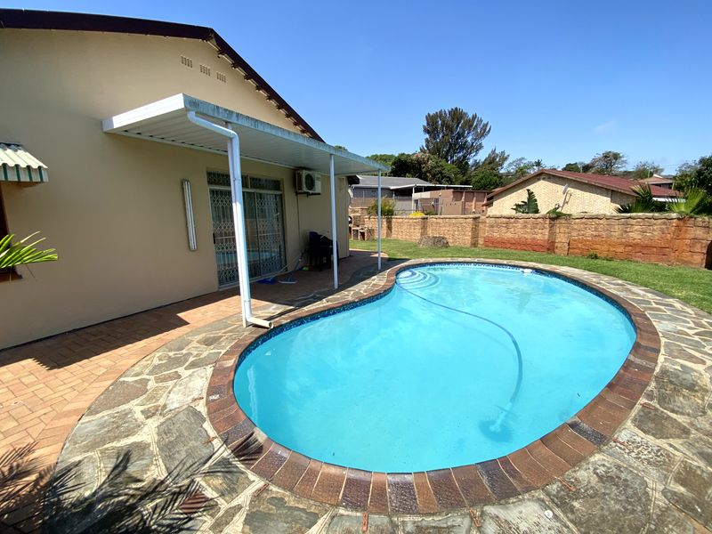 Outdoor pool area featuring a kidney-shaped swimming pool, stone paving, and a covered patio area adjacent to the main house.