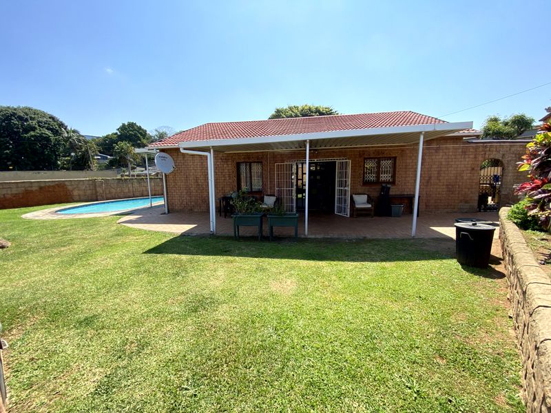 Rear view of the property featuring a covered patio, brick facade, and a swimming pool set within a landscaped garden.