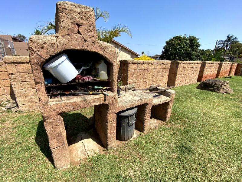 Outdoor garden area featuring a built-in stone braai and perimeter stone walling set within a grassed yard.