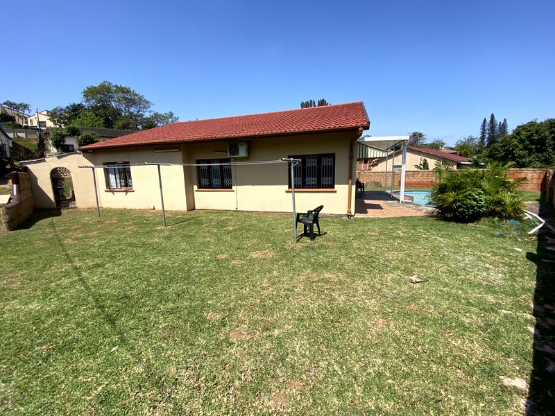 Rear view of the house featuring a lawn, swimming pool, and patio area with security bars on windows.