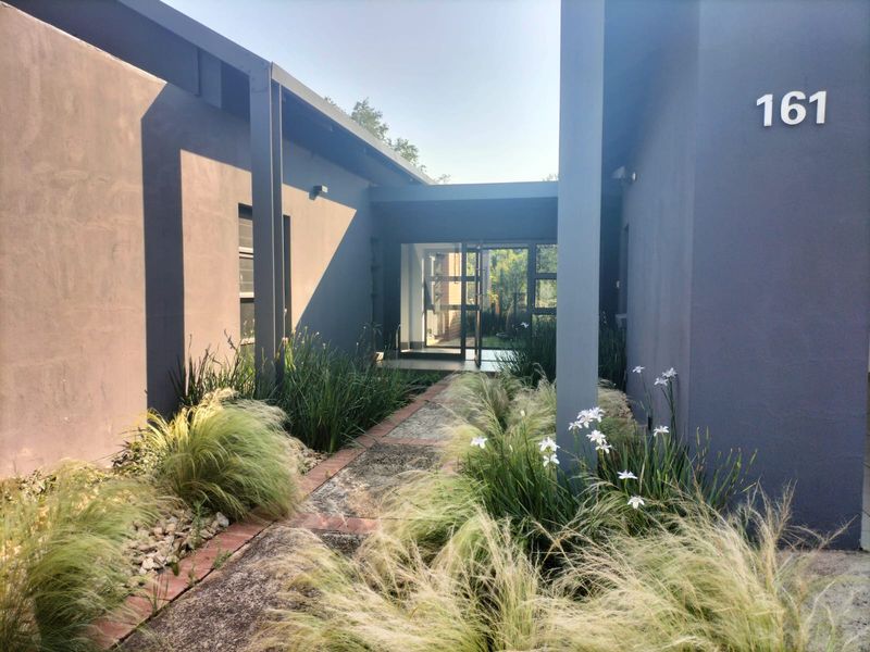 Modern front entrance featuring a paved walkway leading to a glass door, framed by contemporary dark-toned exterior walls and landscaped garden beds.