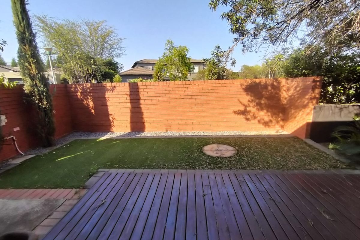A private rear garden featuring a timber deck, artificial lawn, and a high brick boundary wall providing privacy.
