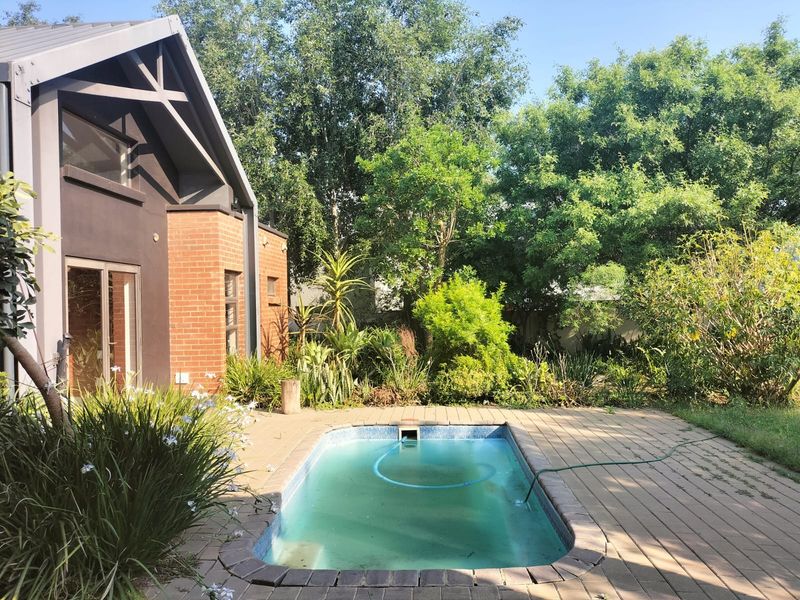Outdoor pool area featuring a swimming pool with brick paving, set against a modern home with exposed brick and timber architectural details.