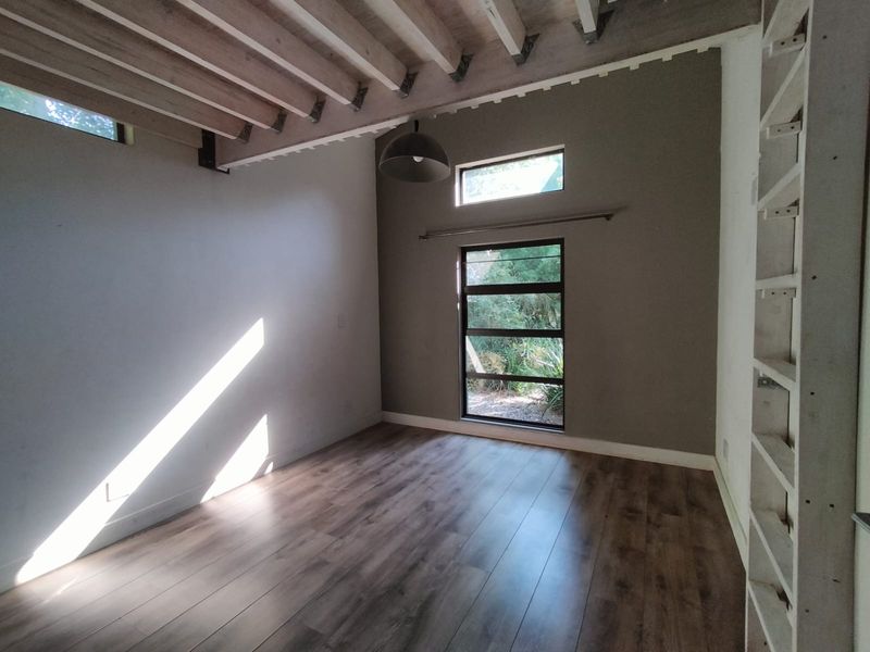 A bright, empty bedroom featuring exposed timber ceiling beams, modern laminate flooring, and large windows that provide ample natural light.