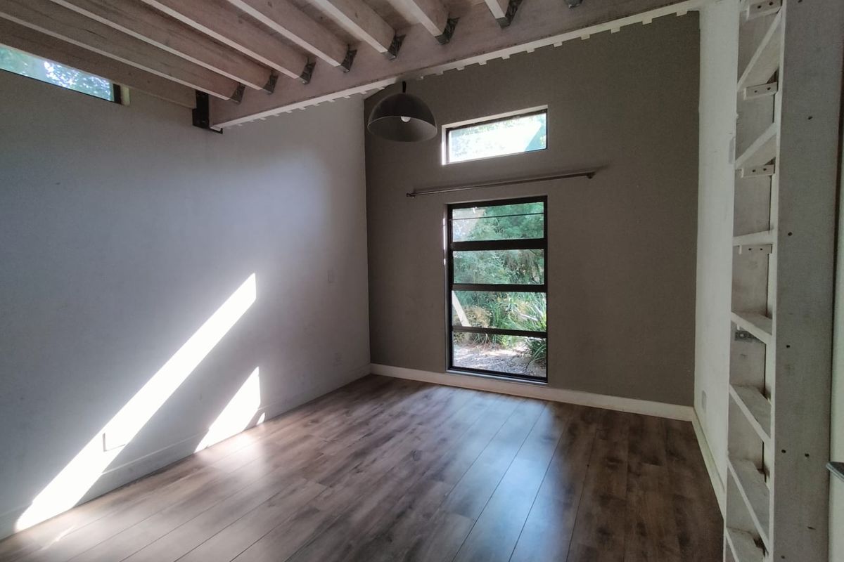 A bright, empty bedroom featuring exposed timber ceiling beams, modern laminate flooring, and large windows that provide ample natural light.