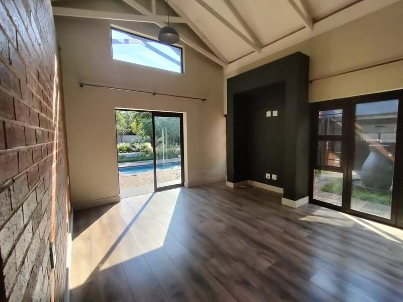 Spacious living room featuring vaulted ceilings, exposed brick wall, laminate flooring, and large sliding doors providing direct access to the pool area.