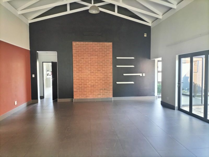 Spacious living area featuring high ceilings with exposed trusses, tiled floors, a brick feature wall, and large sliding glass doors leading outdoors.