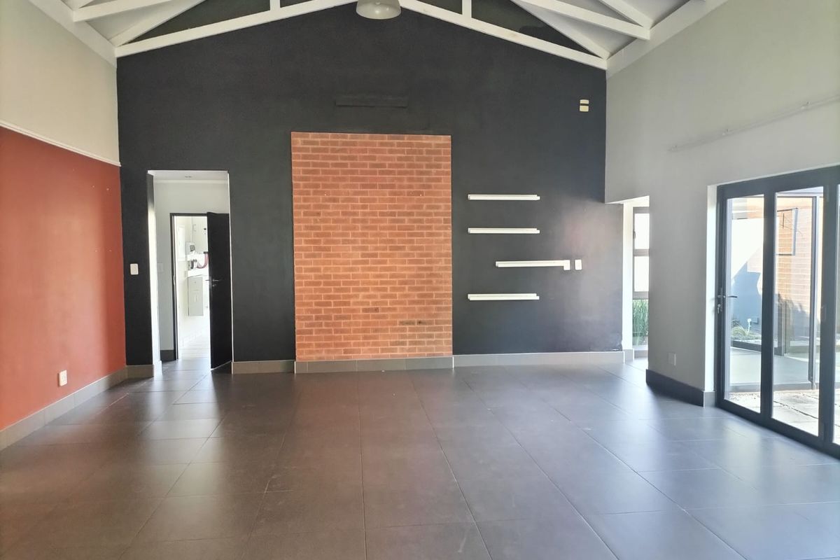 Spacious living area featuring high ceilings with exposed trusses, tiled floors, a brick feature wall, and large sliding glass doors leading outdoors.