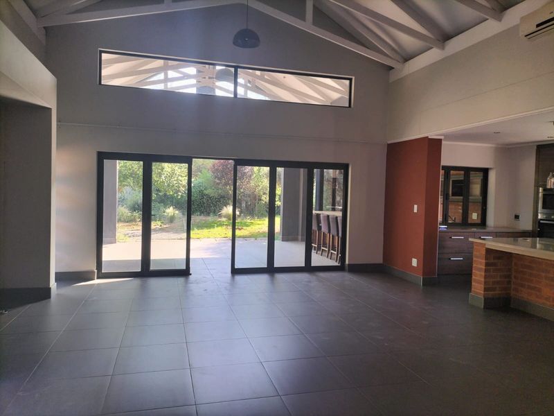 Spacious open-plan living area featuring vaulted ceilings with exposed rafters, large sliding doors to the garden, and a functional kitchen with brick island base.