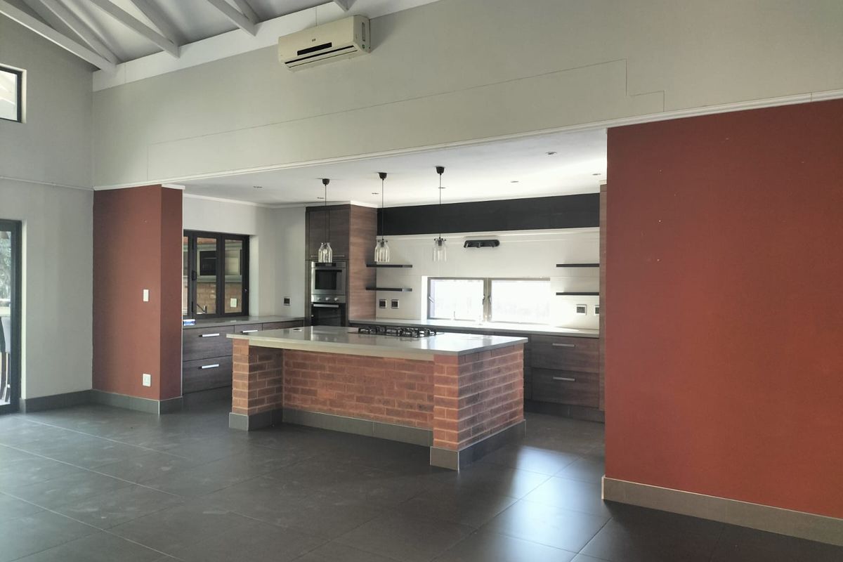 Spacious kitchen featuring a central brick-base island, built-in oven, gas hob, and vaulted ceilings, finished with modern dark cabinetry and tiled flooring.