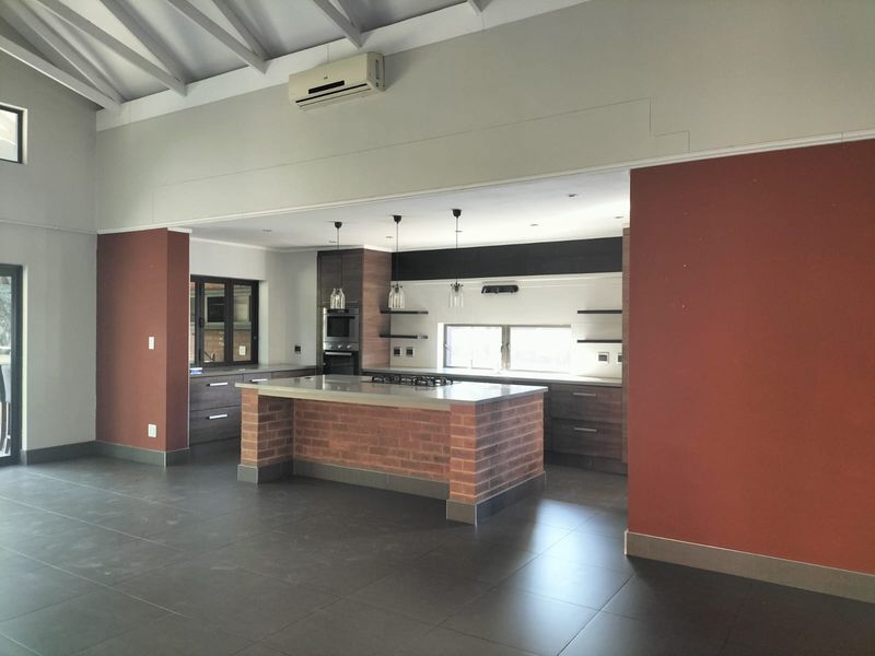 Spacious kitchen featuring a central brick-base island, built-in oven, gas hob, and vaulted ceilings, finished with modern dark cabinetry and tiled flooring.