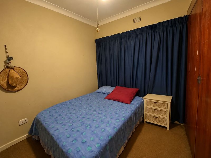 A functional bedroom featuring a built-in wooden wardrobe, neutral wall finishes, and carpeted flooring.