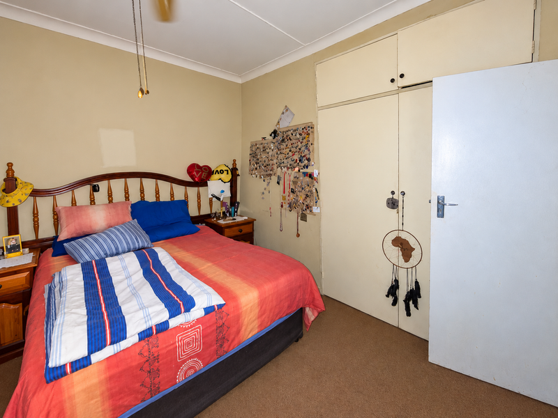 A bedroom featuring built-in cupboards, a ceiling fan, and carpeted flooring. The space offers a functional layout with potential for cosmetic updates.