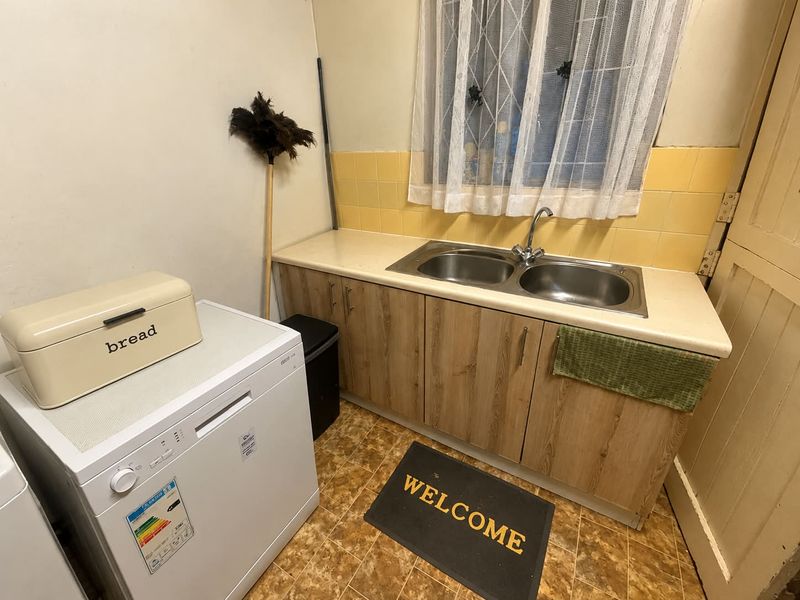 A functional laundry area featuring a double bowl stainless steel sink, laminate countertops, wood-look cabinetry, and yellow tiled splashbacks.