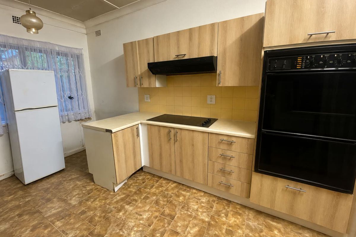 A functional kitchen featuring light wood-look cabinetry, built-in oven, electric cooktop, and tiled backsplash, offering a practical layout with potential for modern updates.