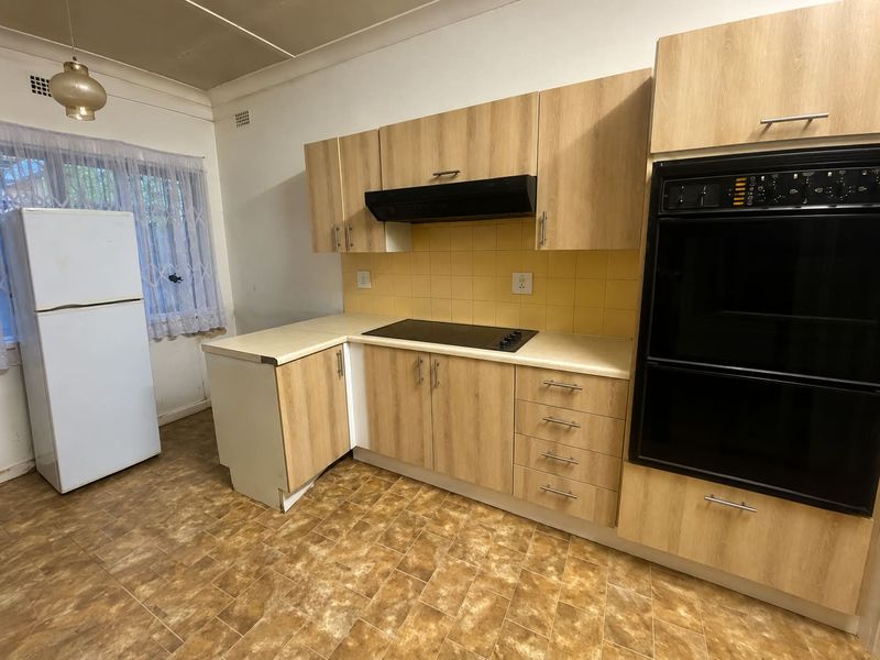 A functional kitchen featuring light wood-look cabinetry, built-in oven, electric cooktop, and tiled backsplash, offering a practical layout with potential for modern updates.