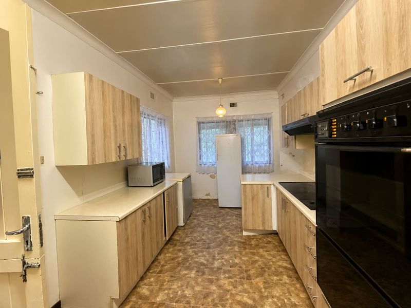 A functional kitchen featuring light wood-look cabinetry, built-in oven and hob, and vinyl flooring. The space offers a practical layout with ample storage.