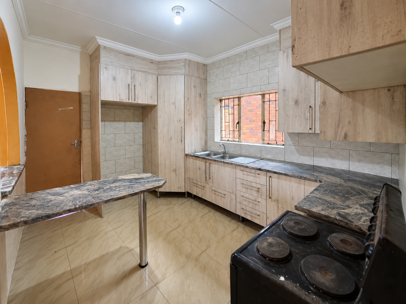 A functional kitchen featuring light wood-look cabinetry, stone-patterned countertops, a breakfast bar, and tiled flooring, offering a clean and practical workspace.