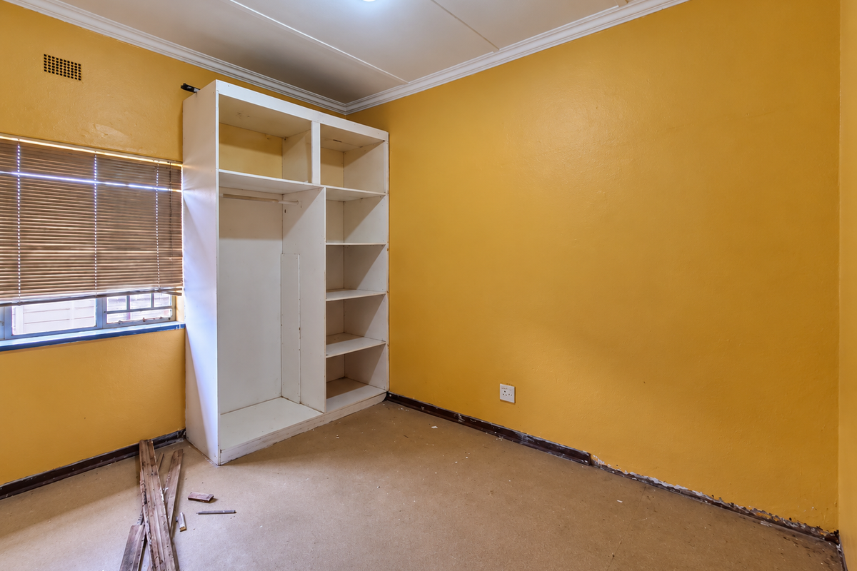 An empty bedroom featuring a built-in wardrobe, venetian blinds, and ceiling cornicing. The room requires flooring and skirting board repairs.