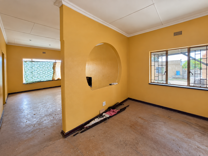 An empty living area featuring a distinctive circular wall cutout, steel-framed windows with security bars, and coved ceilings, offering a blank canvas for renovation.