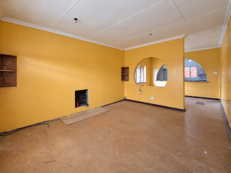 An empty open-plan living area featuring yellow walls, a built-in fireplace, and a distinctive arched opening leading to the kitchen space.