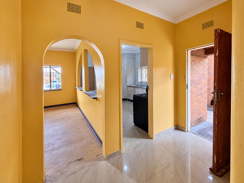 A bright hallway featuring arched architectural details, tiled flooring, and direct access to the kitchen and exterior brick patio area.