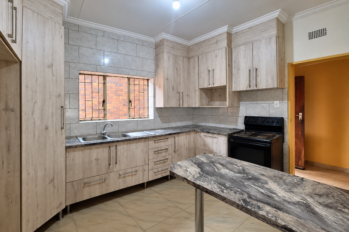 A clean, modern kitchen featuring light wood-grain cabinetry, stone-look countertops, a double sink, and a freestanding electric stove with tiled backsplash.