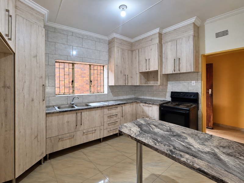 A clean, modern kitchen featuring light wood-grain cabinetry, stone-look countertops, a double sink, and a freestanding electric stove with tiled backsplash.