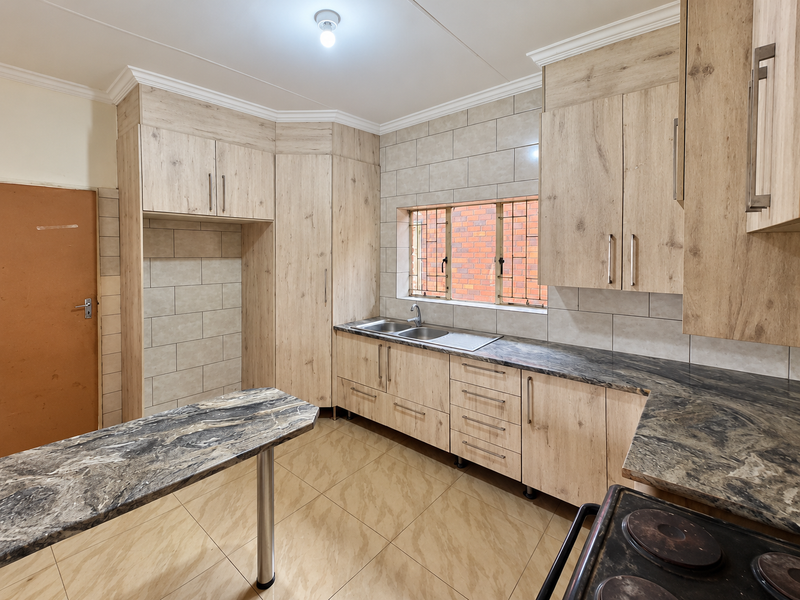 A functional kitchen featuring light wood-look cabinetry, dark stone-effect countertops, tiled backsplash, and a convenient breakfast nook area.