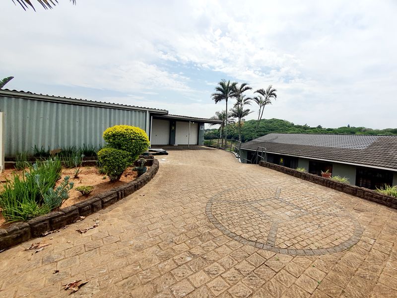 Spacious paved driveway leading to a double garage with a well-maintained stone retaining wall and landscaped garden area.