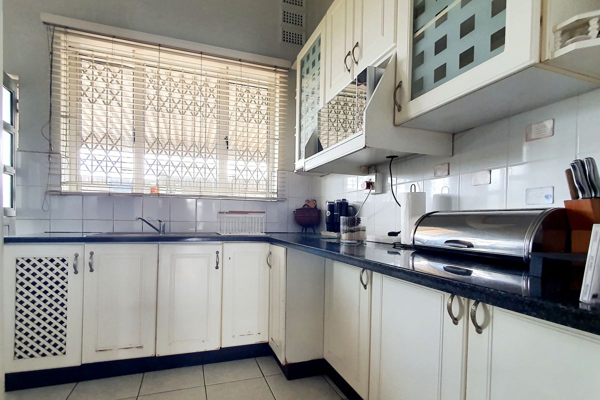 A functional kitchen featuring white built-in cabinetry, dark laminate countertops, tiled backsplash, and a window with security bars.