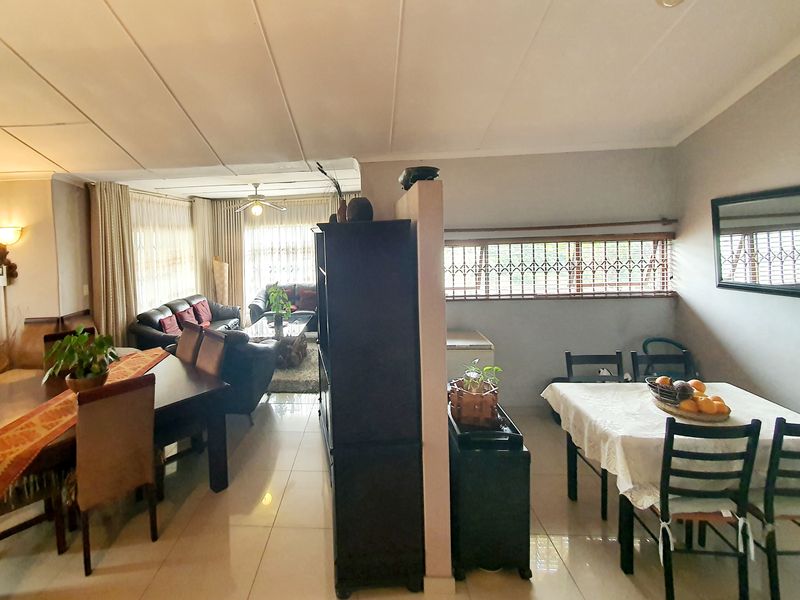 Spacious open-plan living and dining area featuring tiled flooring, a central partition wall, and security bars on the windows.