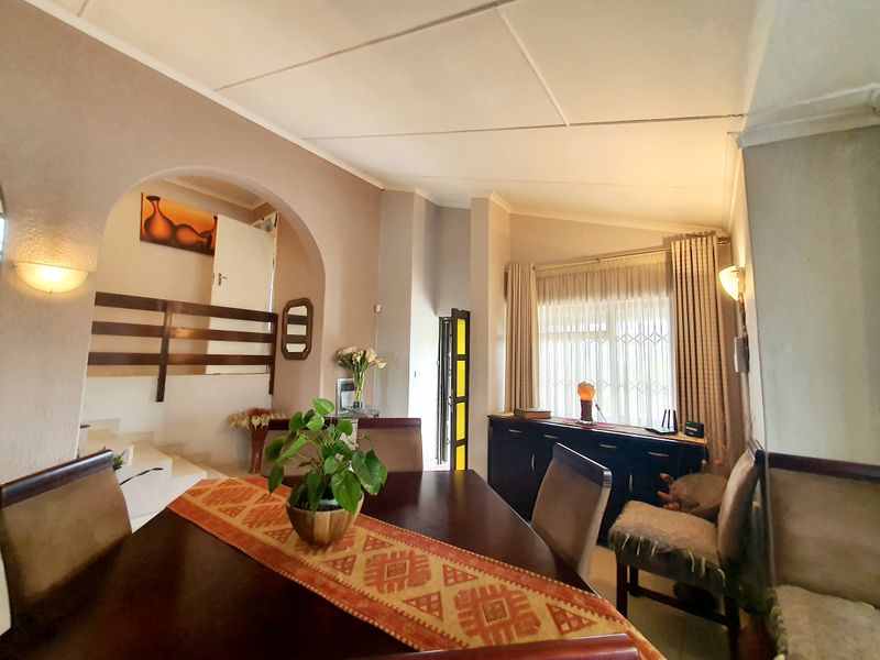 Dining area featuring an arched entryway, staircase with wooden balustrade, and large window with security bars, providing a functional and connected living space.