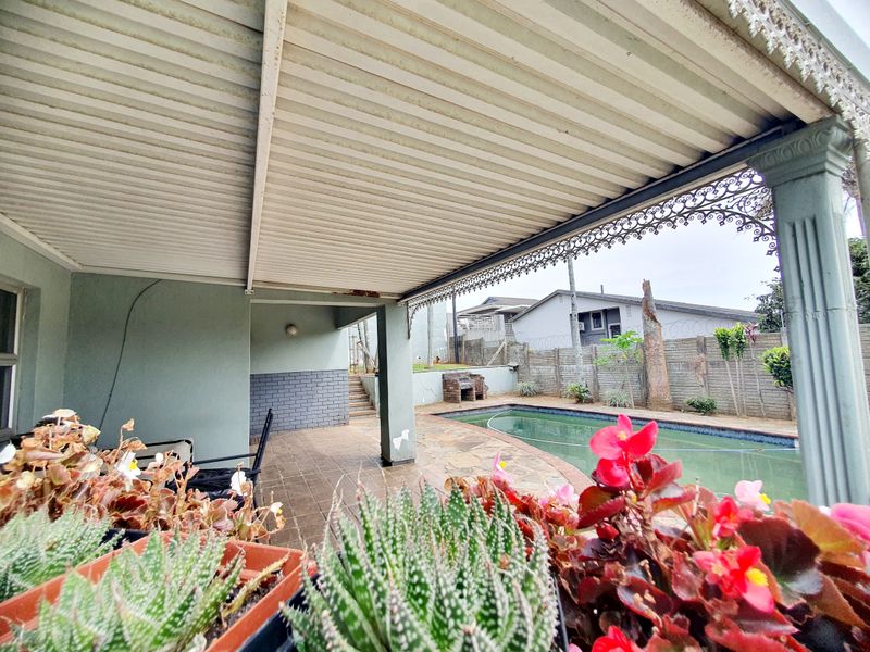 Covered patio area featuring tiled flooring and decorative wrought iron trim, overlooking a swimming pool and private garden with brick boundary walling.