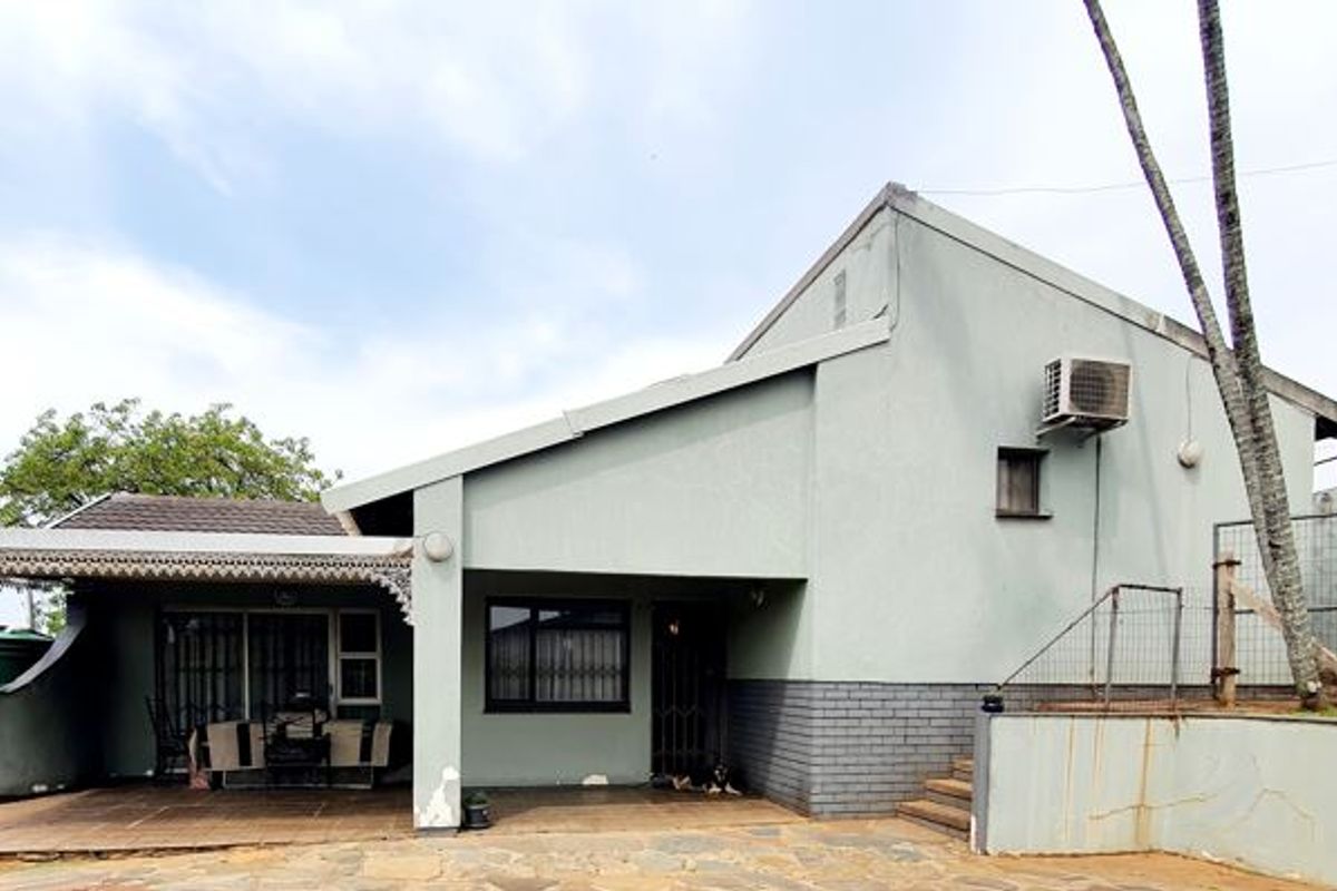 Rear exterior view of the property featuring a covered patio area, paved courtyard, and functional outdoor infrastructure including a water tank and air conditioning unit.