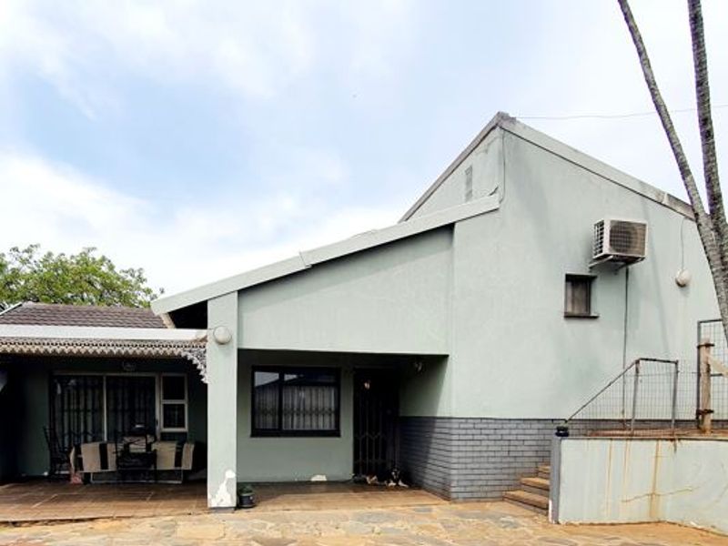 Rear exterior view of the property featuring a covered patio area, paved courtyard, and functional outdoor infrastructure including a water tank and air conditioning unit.