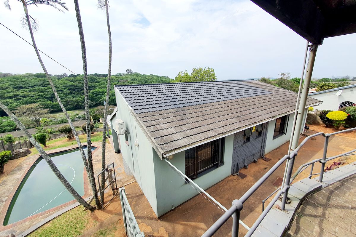 Aerial view of the property featuring a tiled roof, swimming pool, and paved outdoor area, overlooking a lush green landscape.