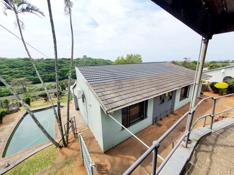 Aerial view of the property featuring a tiled roof, swimming pool, and paved outdoor area, overlooking a lush green landscape.