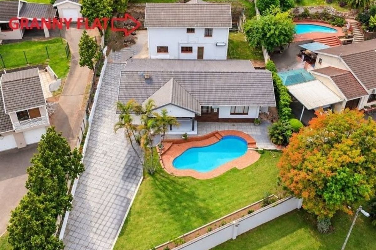 Aerial view of a residential property featuring a swimming pool, paved driveway, detached garage, and well-maintained garden areas.