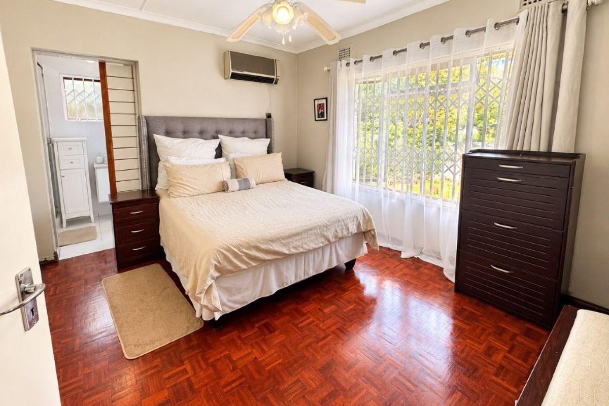 A well-maintained bedroom featuring classic parquet flooring, a ceiling fan, and an integrated air conditioning unit, with an adjoining en-suite bathroom.