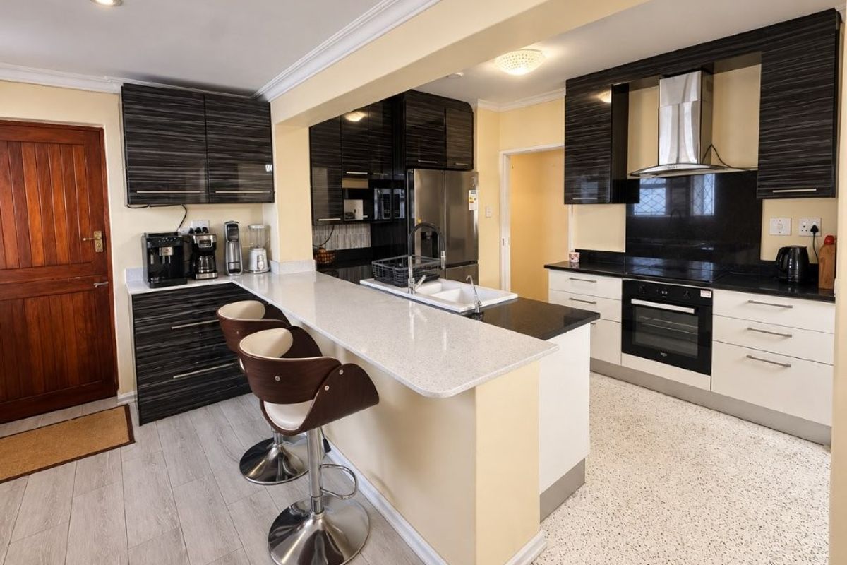Modern kitchen featuring high-contrast cabinetry, stone countertops, a breakfast bar, and integrated appliances, offering a functional and stylish culinary space.